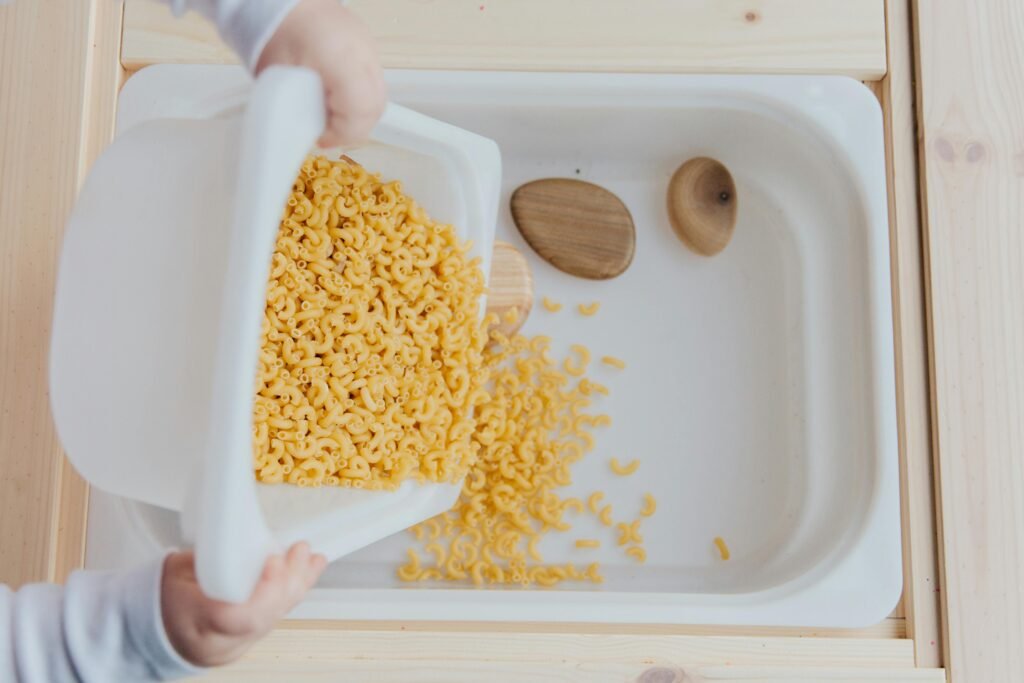 A child engages in a fun and educational sensory activity with uncooked macaroni.