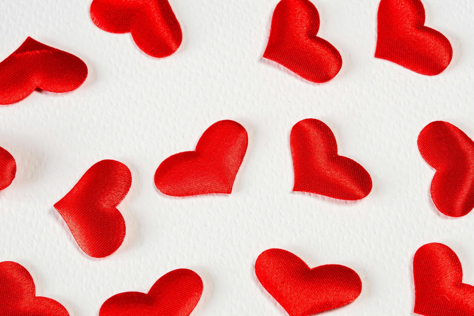 Red satin heart shapes scattered on a white textured background, perfect for Valentine's Day themes.